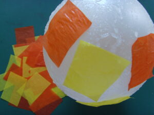 Collage des premiers morceaux de papier de soie orange et jaune sur le ballon