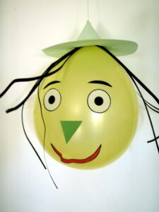 Tête de sorcière rigolote jaune fabriquée avec un ballon de baudruche, un chapeau pointu en papier et des cheveux noirs pour un bricolage d'Halloween d'enfants.
