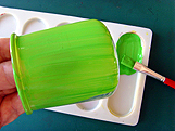 Application de peinture verte au pinceau sur un pot en verre de yaourt.
