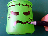 Marqueur noir dessinant la bouche et les cicatrices de Frankenstein sur le pot peint en vert.
