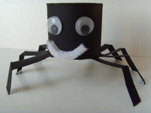 Araignée d'Halloween fabriquée avec un rouleau de papier toilette peint en noir, des yeux mobiles et un sourire en cure-pipe blanc.